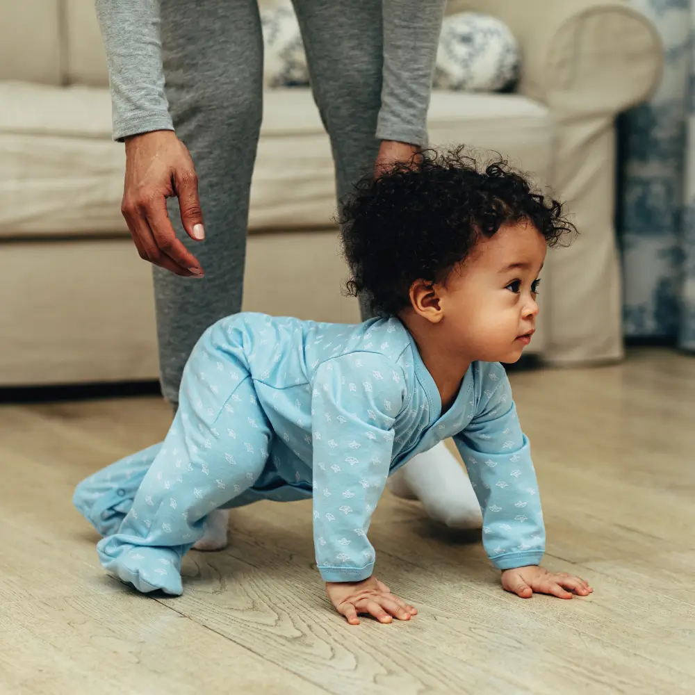 bipoc mother helps bipoc baby with natural hair start crawling on wood floor. represents how crawling is important for brain development.
