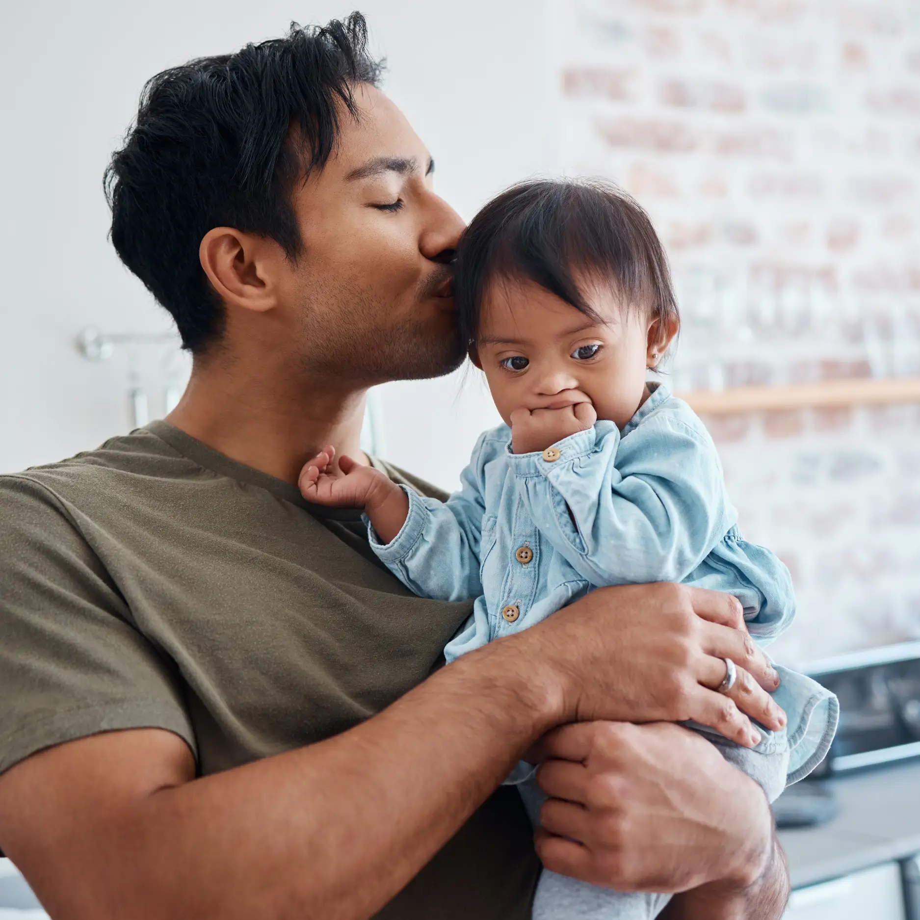 dad holds and kisses his special needs downs syndrome infant son to represent crawlaroo best tummy time toy for motor skills development delays special needs infants